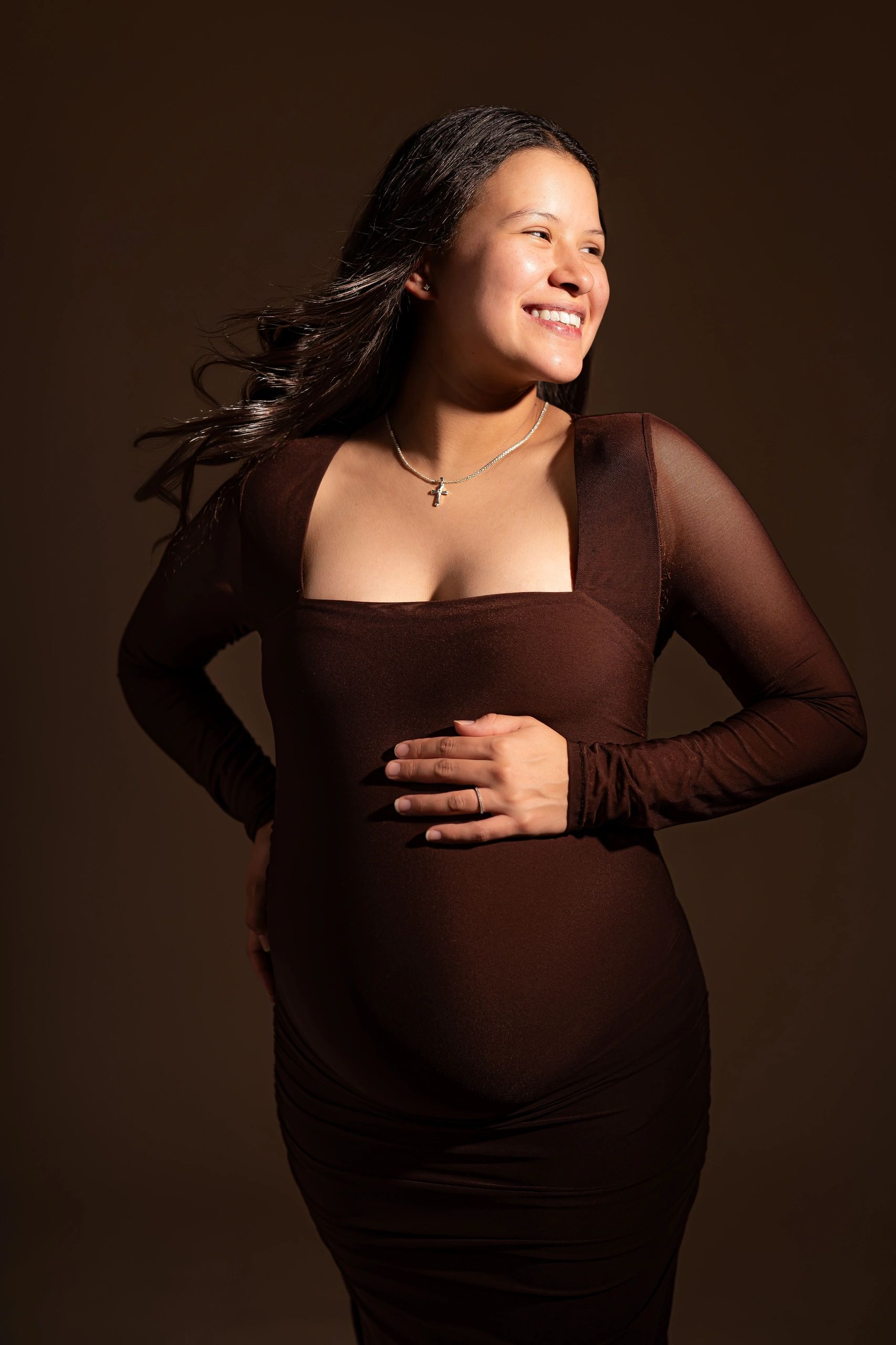 Smiling pregnant woman in brown dress with flowing hair.