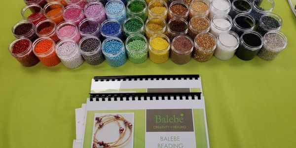 Colorful beads in small containers with Balebe beading guides on a green table.