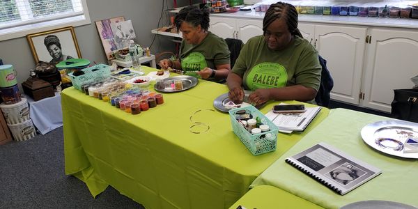 Two women sit at a table engaged in beadwork and crafting activities.