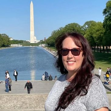 Woman smiling near the Reflecting Pool with the Washington Monument in the background.