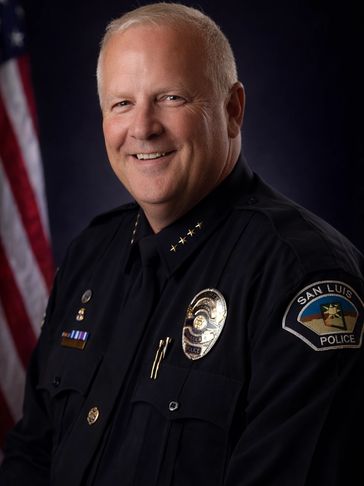 Police officer in uniform with San Luis Police badge and American flag background.