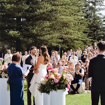 Elizabeth officiating at her first wedding. Bride & groom with friends and family in the background