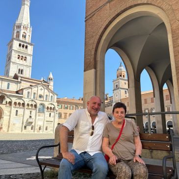 A man and woman sitting on a bench in a historic square.