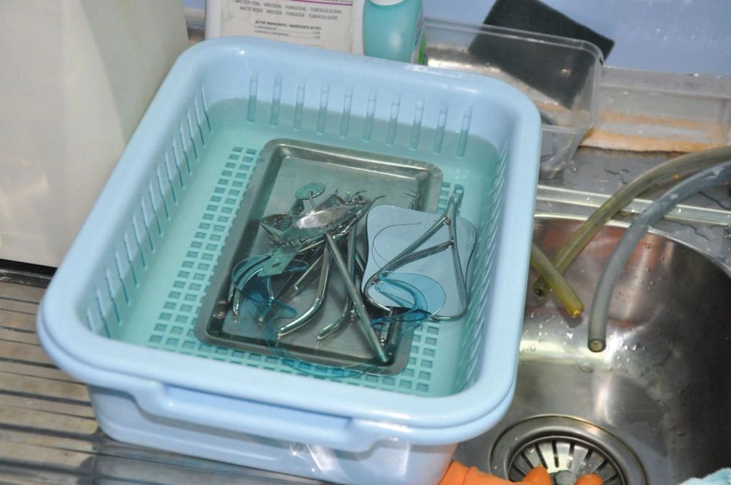 Sterilizing medical instruments soaking in a blue plastic basin filled with water.