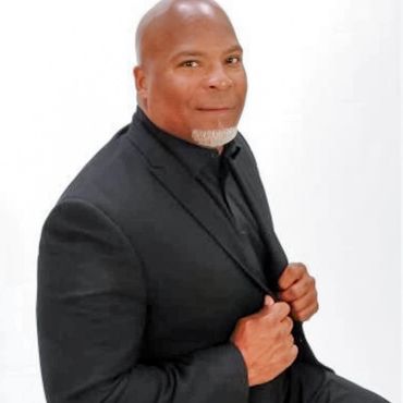Man in black suit with white beard posing.