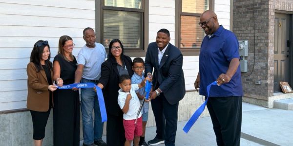 Group cutting ribbon at a ceremony outside a building.