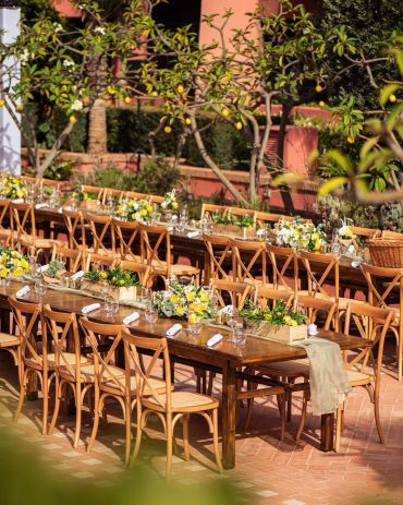 Outdoor rustic dining tables with wooden chairs and floral centerpieces.