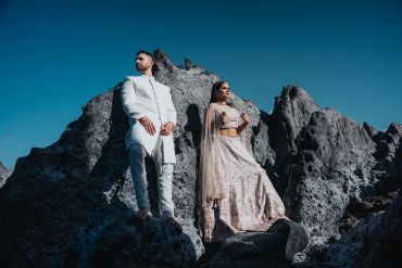 Couple in traditional attire posing on rocks under blue sky.