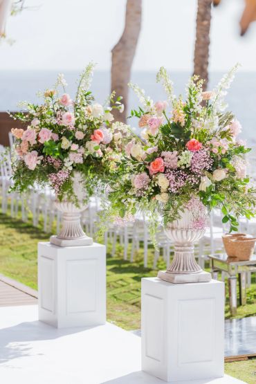 Elegant floral arrangements in white urns at an outdoor event.