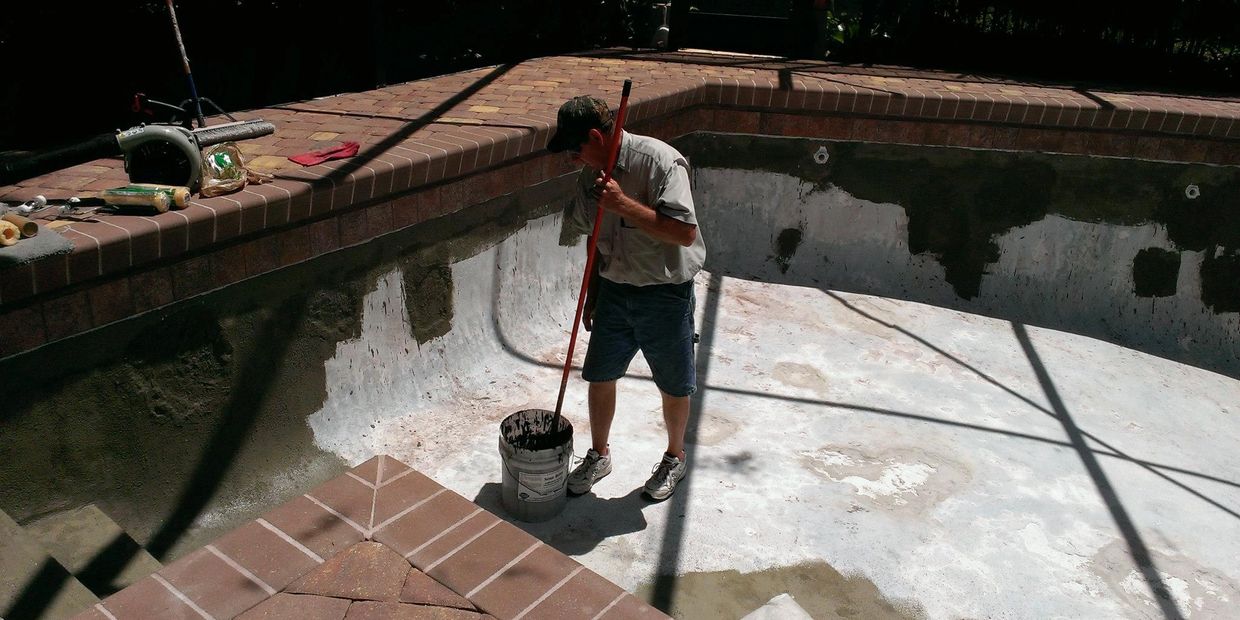 Man working inside an empty pool, stirring a bucket of material.