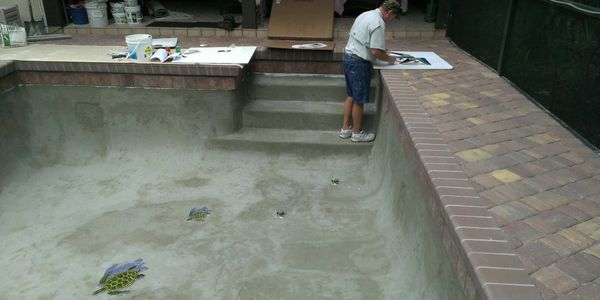 A man paints inside an empty swimming pool with turtle designs on the floor.