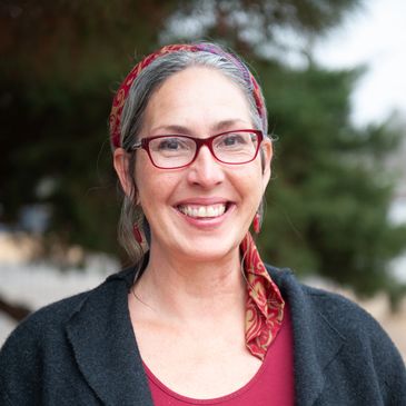 Smiling woman wearing red glasses and a patterned headscarf outdoors.