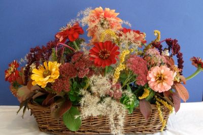 Colorful flower arrangement in a wicker basket against a blue background.