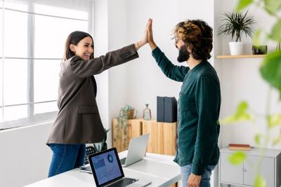 Two coworkers giving each other a high five in an office.