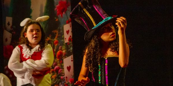 Duas pessoas em um cenário teatral, uma com orelhas de coelho.