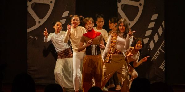 Grupo de seis jovens atuando em palco com figurino criativo.