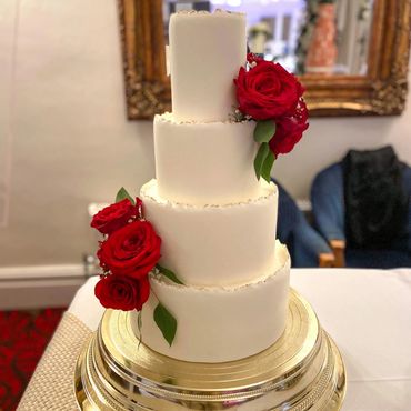 4 tier fondant wedding cake with gold edging and red roses.
