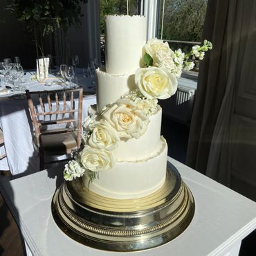 4 tier fondant wedding cake with white florals cascading down cake on an angle.