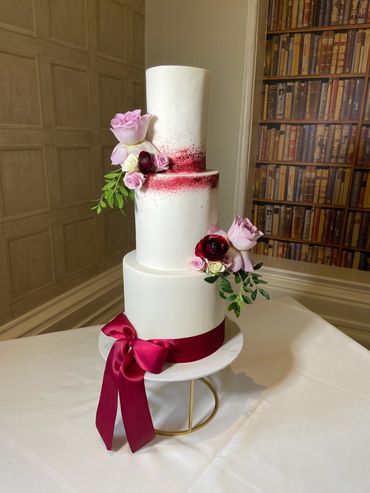 3 Tier white wedding cake with burgundy ribbon.