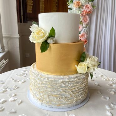 Three tier wedding cake. White top, gold middle and bottom tier with ruffles.
