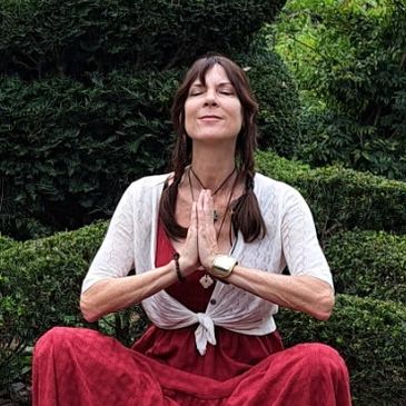 Woman meditating in front of a large Buddha-shaped topiary.