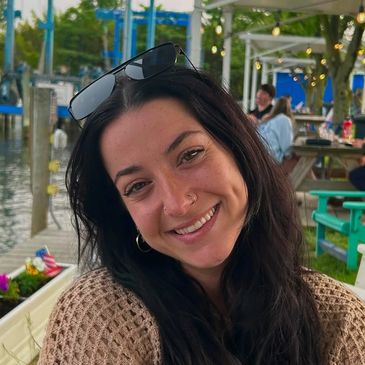 Smiling young woman sitting outdoors by the water on a cozy day.