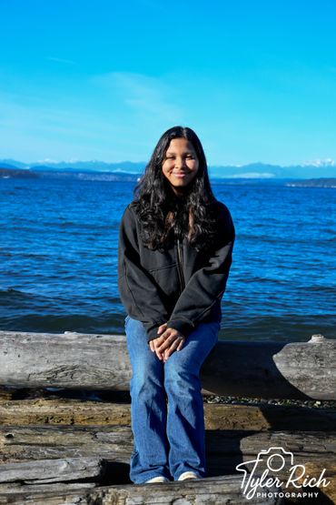 Young woman sitting on driftwood by the ocean on a clear sunny day.