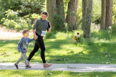 A woman and a young boy walking outdoors in a park on a sunny day.