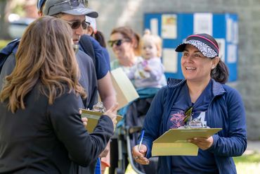Volunteers interact while holding clipboards outdoors at an event.