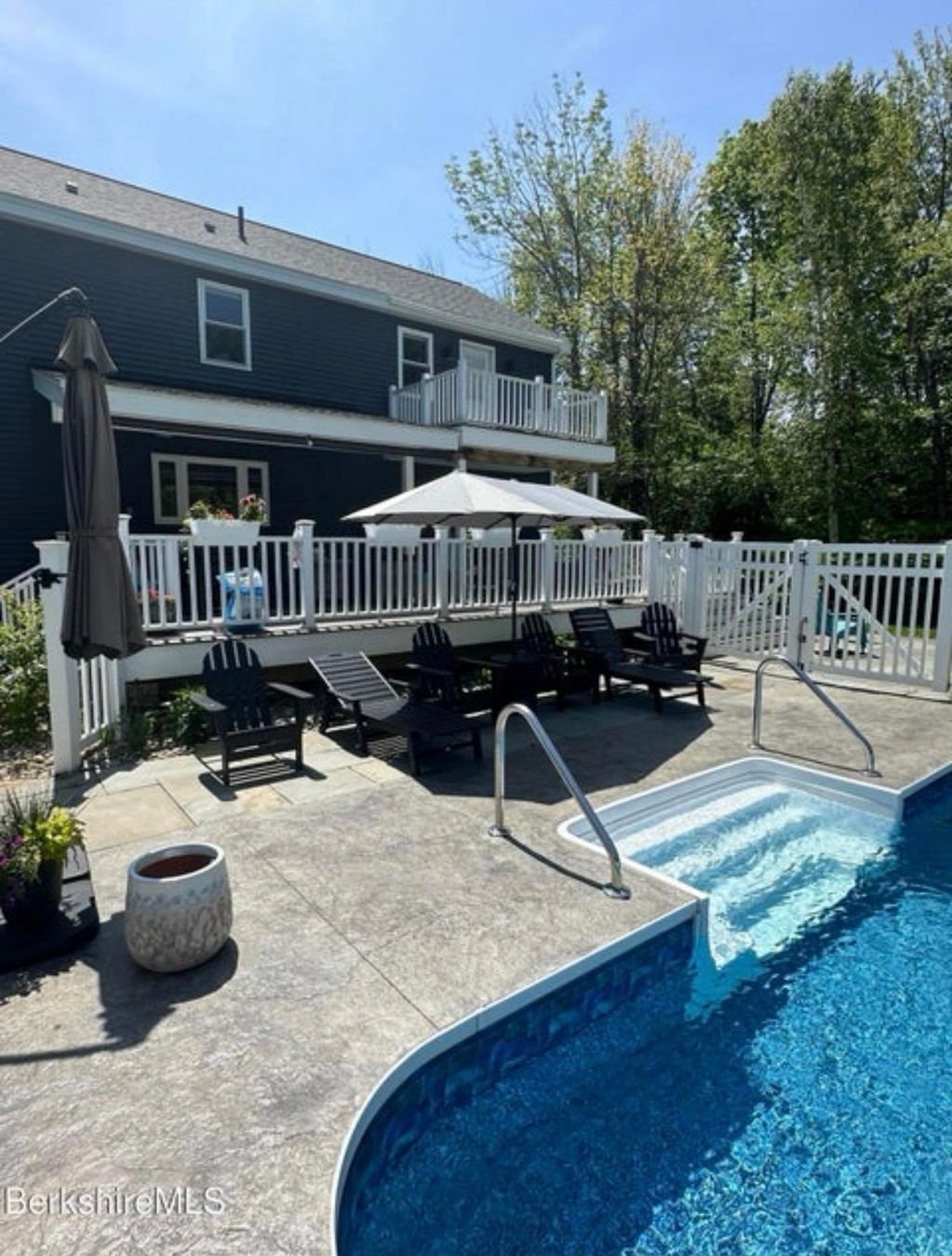 Backyard pool area with lounge chairs and umbrellas next to a dark blue house.