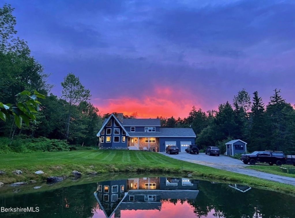 A serene house by a pond with a vibrant sunset reflecting in the water.