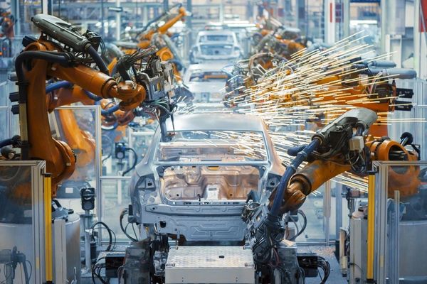 Robotic arms assembling and welding a car frame in a factory.