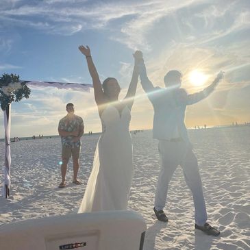 Newlyweds celebrate joyfully on a sunny beach at sunset.