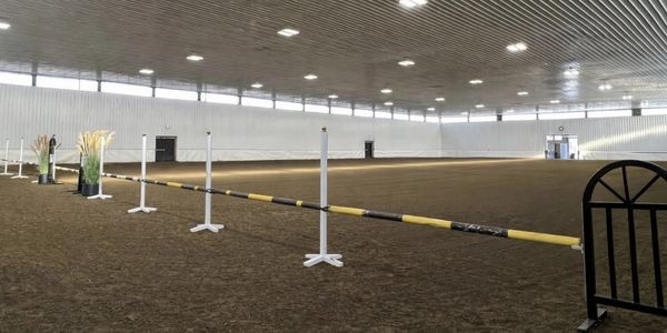 Indoor equestrian arena with jumping obstacles and wide space.