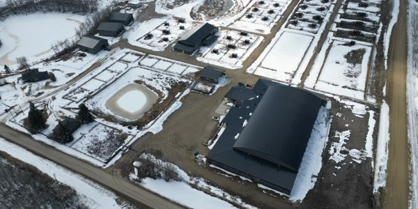 Aerial view of a snowy farm with multiple buildings and fenced areas.