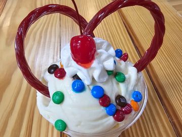 Cup of ice cream with whipped cream, M&amp;Ms, and licorice sticks.
