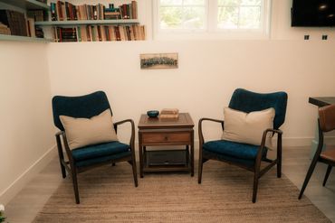 Two blue armchairs with beige pillows flank a wooden side table in a cozy reading nook.