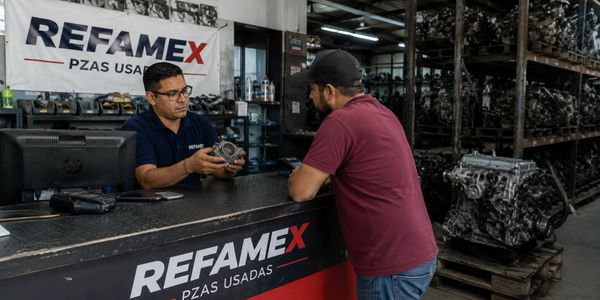 Two men discussing a car part at a used auto parts store counter.