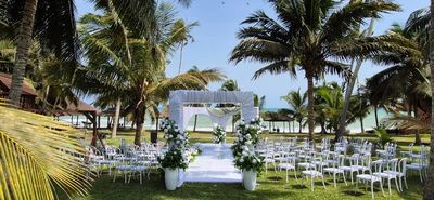 Outdoor wedding setup with white chairs and floral decorations under palm trees.