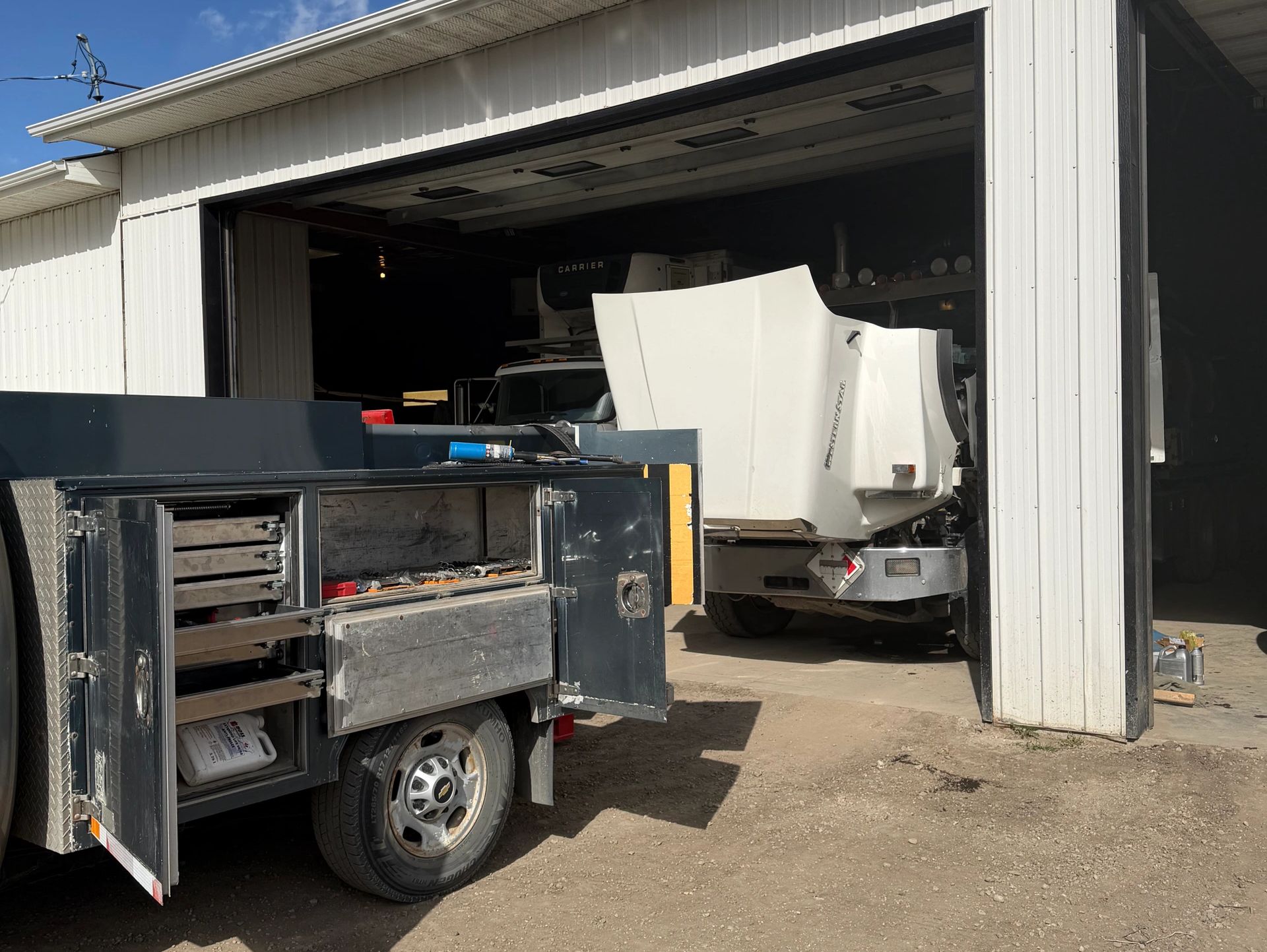 Truck with open tool compartments and a white tractor unit in a garage.