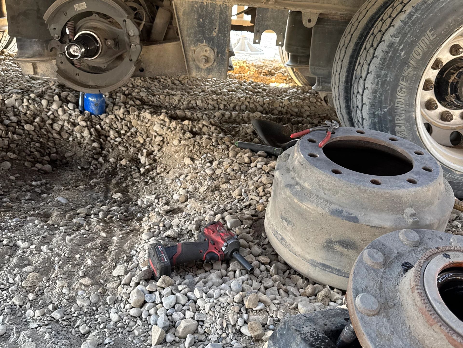 Truck wheel removed for repair on rocky ground with tools scattered nearby.