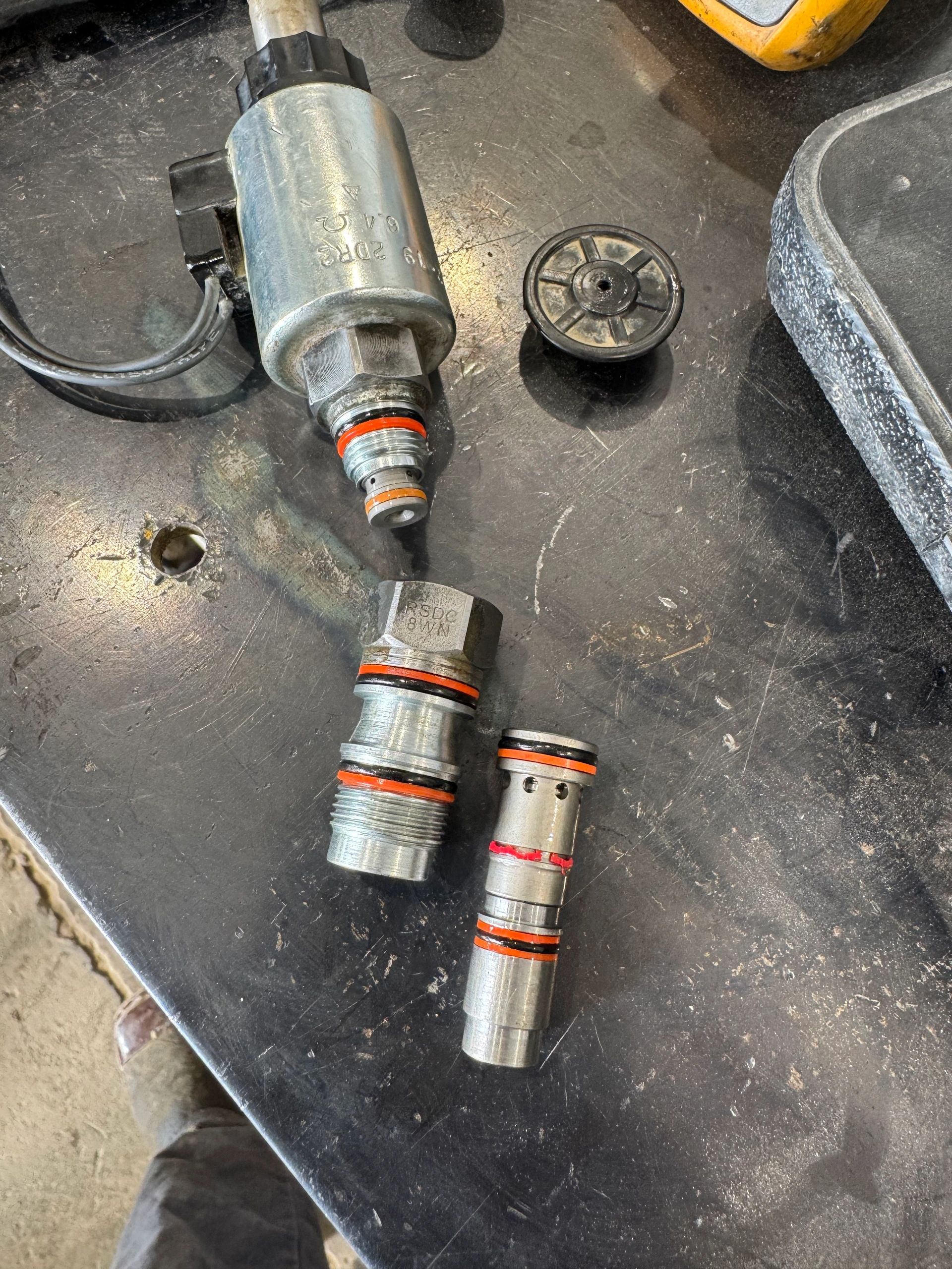 Various metal hydraulic or pneumatic components with orange and black sealing rings on a workbench.