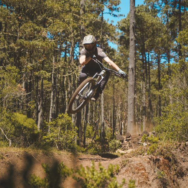A mountain biker jumps mid-air on a forest trail.  Putting mountain bike suspension to the test.
