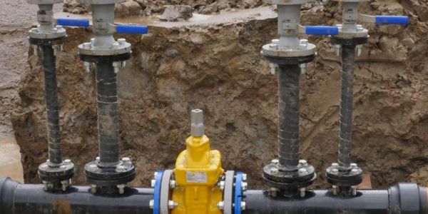 Industrial water pipes and valves installed in a muddy construction trench.