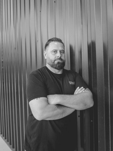 Man with beard and crossed arms leaning against metal wall.
