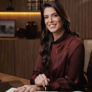 Smiling woman in a maroon blouse sitting at a desk with documents.