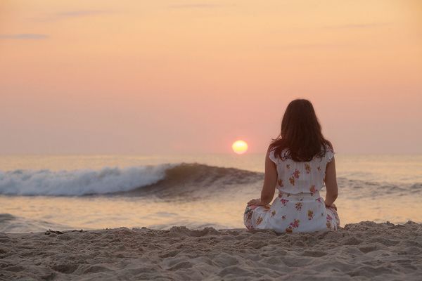 Woman in floral dress watches sunset over ocean waves at the beach.