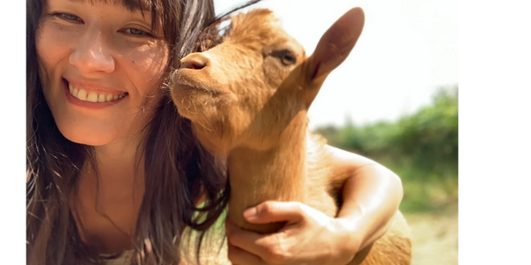 A woman smiling while holding a brown goat close to her face.