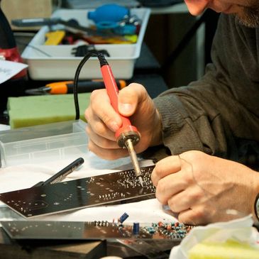 Señor usando un cautín para arreglar un equipo electrónico 