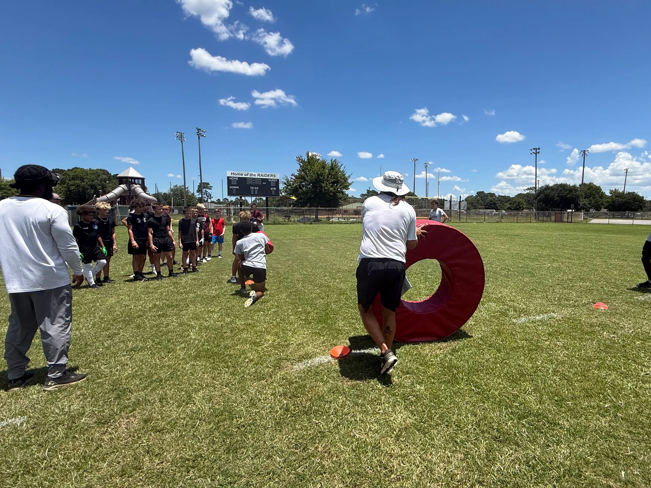 Coach training young athletes on a sunny football field.